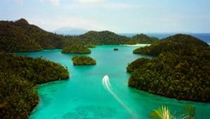 A speedboat’s wake throws relief against the aquamarine, turquoise and emerald shades of the Wajag lagoon, Raja Ampat, Indonesia